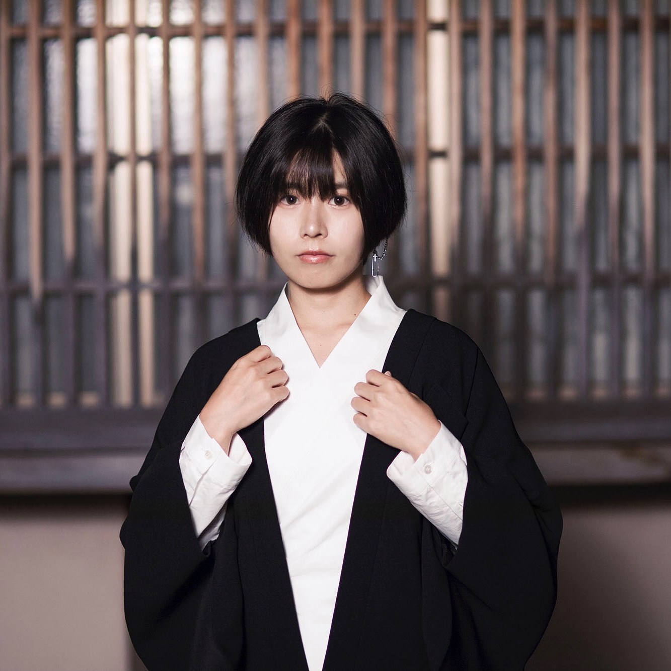 格子の前で、白のSamurai Mode Shirtに黒のJacketを重ねた女性